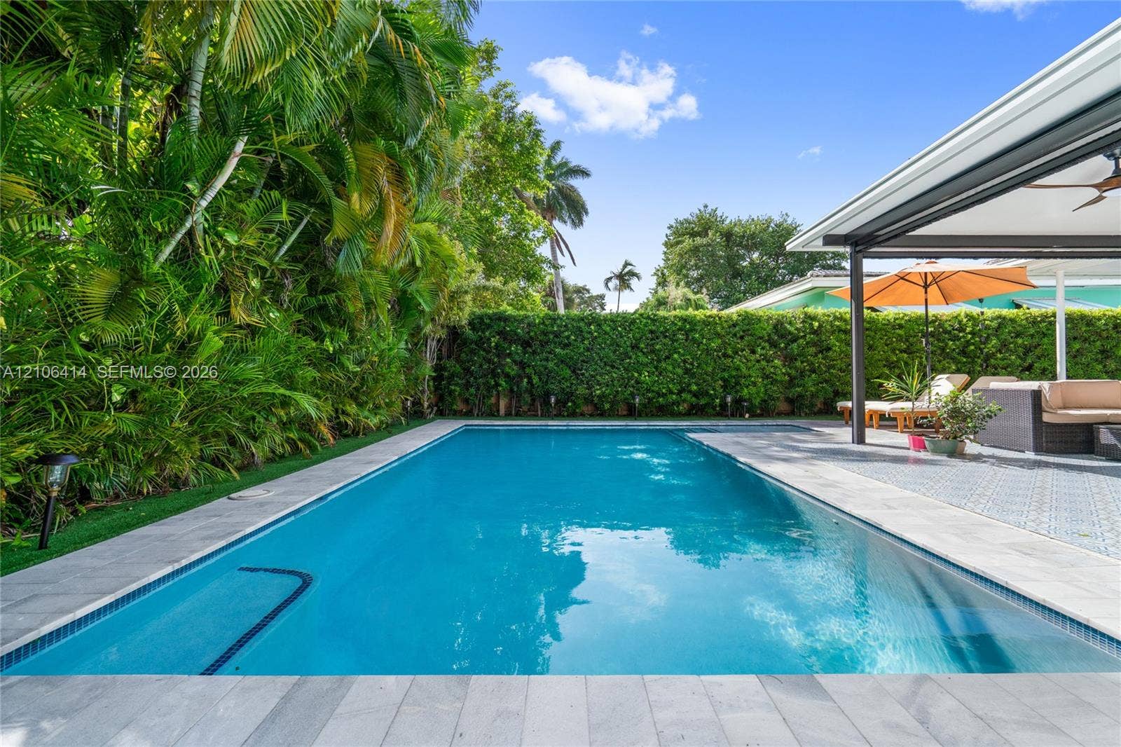 9133 Garland Avenue, Surfside, FL 33154 In-ground swimming pool with stone-tiled decking, covered patio with patterned flooring, and perimeter privacy hedging