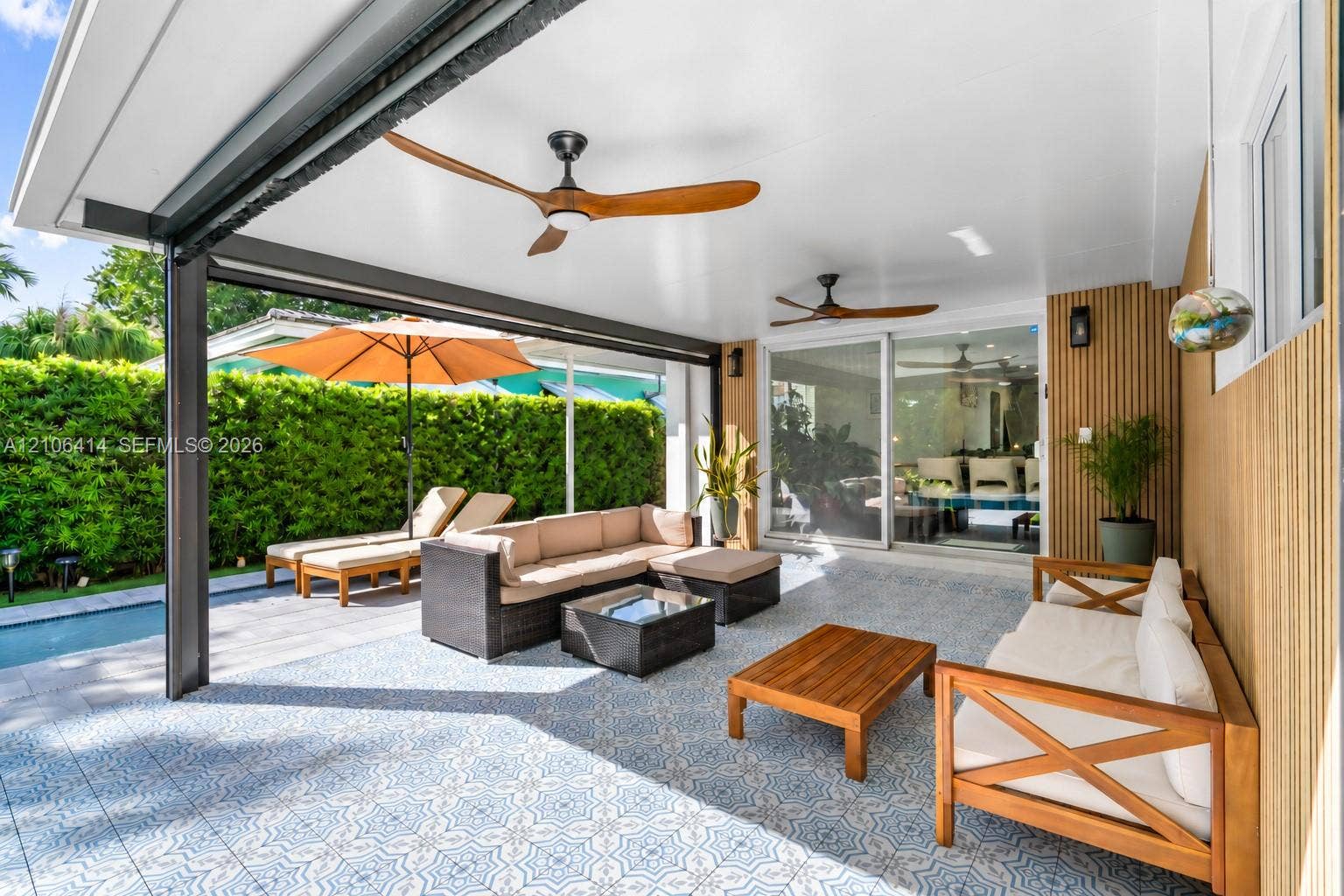 9133 Garland Avenue, Surfside, FL 33154 Covered patio featuring patterned tile flooring, wood-slat accent wall, and two ceiling fans