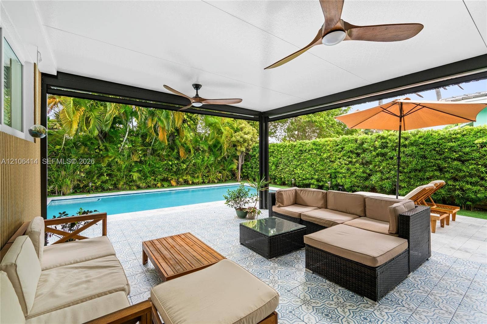 9133 Garland Avenue, Surfside, FL 33154 Covered outdoor patio featuring patterned tile flooring, dual wooden-blade ceiling fans, and a rectangular swimming pool surrounded by a tall hedge
