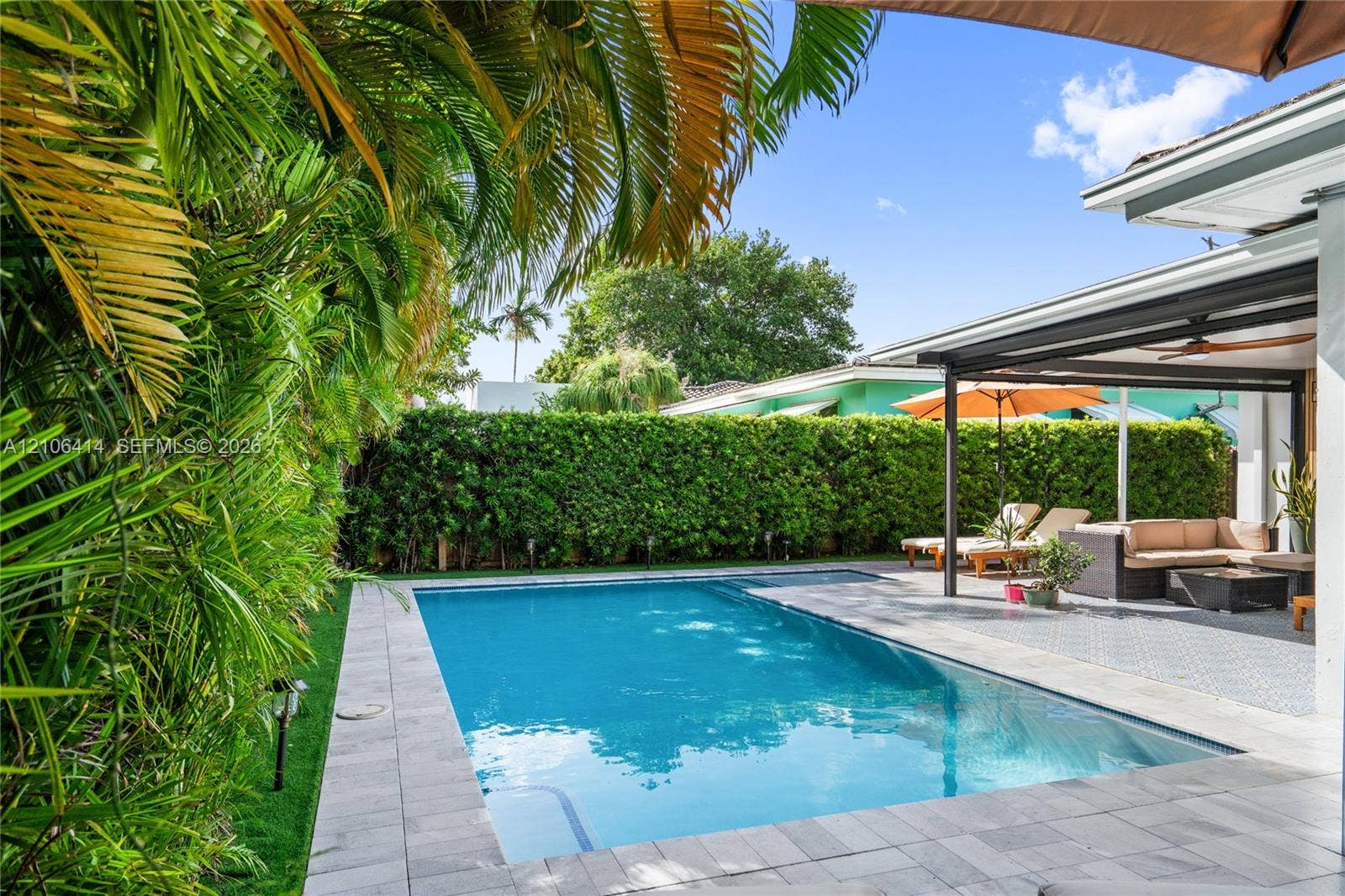 9133 Garland Avenue, Surfside, FL 33154 In-ground swimming pool featuring a stone-paver deck, covered lanai, and surrounding privacy hedges
