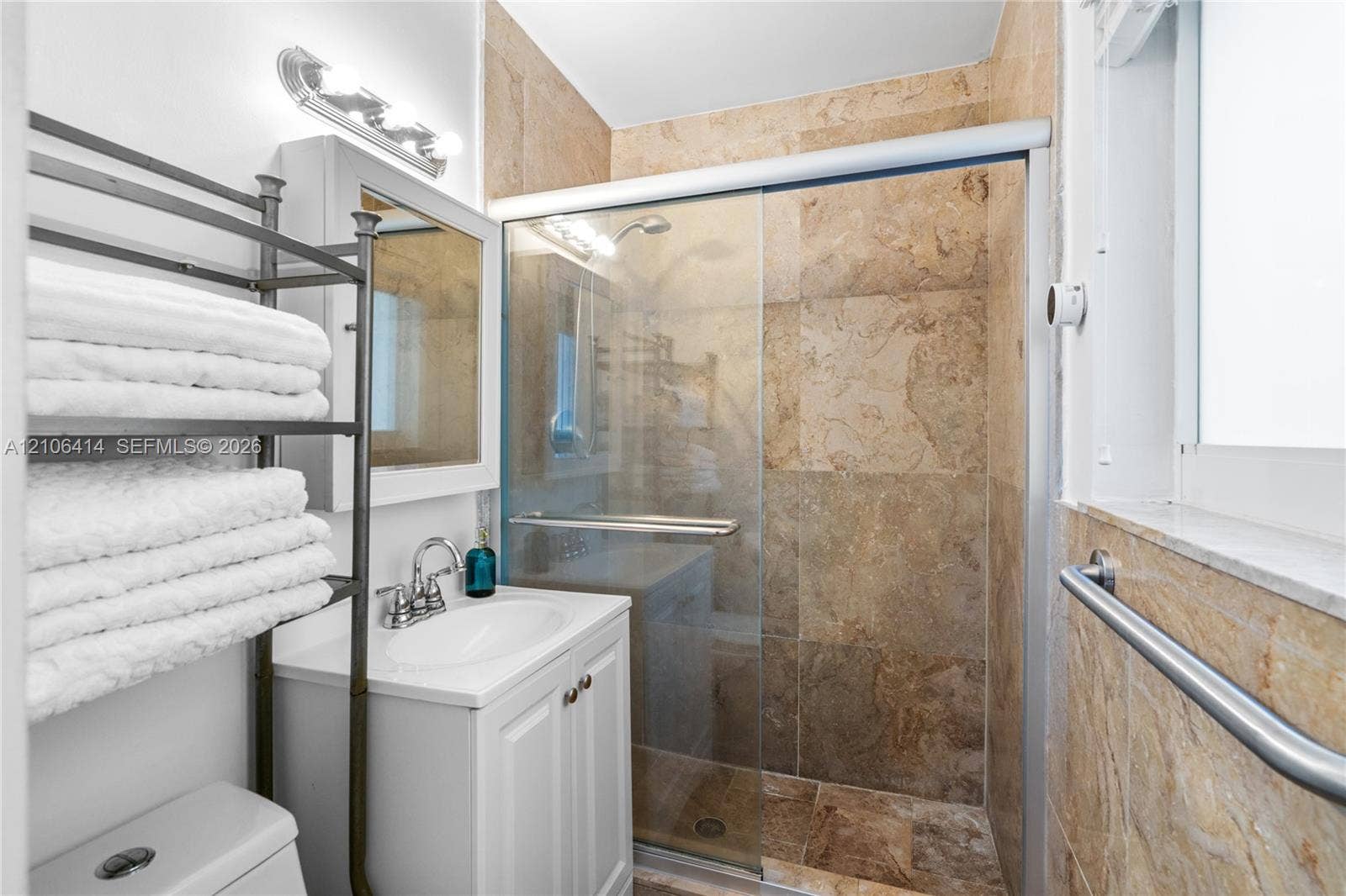 9133 Garland Avenue, Surfside, FL 33154 Bathroom featuring a white vanity cabinet with an integrated sink, a glass-enclosed shower with full-height stone-finish tile surround, and an attached wall-mounted metal grab bar