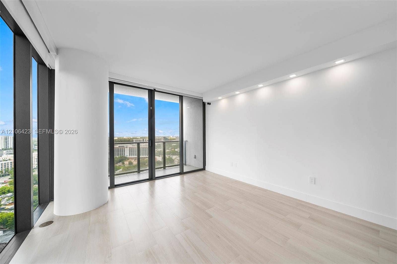Floor-to-ceiling windows, wood-finish flooring, recessed ceiling lighting, and a private balcony featuring a metal railing