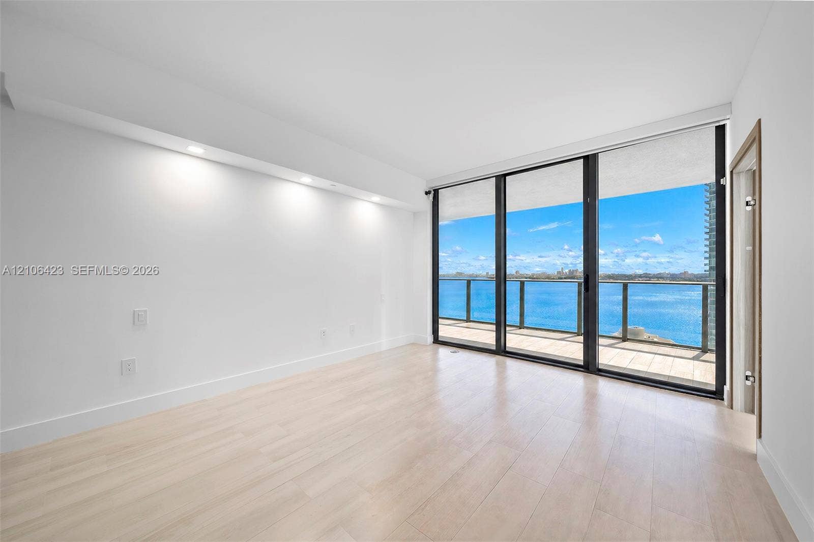 Floor-to-ceiling windows, wood-finish flooring, recessed ceiling lighting, and a private balcony featuring a water backdrop