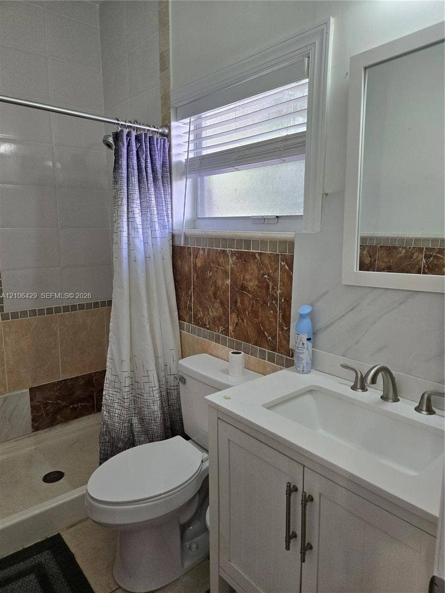 5712 Hollywood Boulevard, #3, Hollywood, Hollywood, FL 33021 White vanity with integrated rectangular sink, stone-finish backsplash, neutral tile wall detailing, and a framed mirror