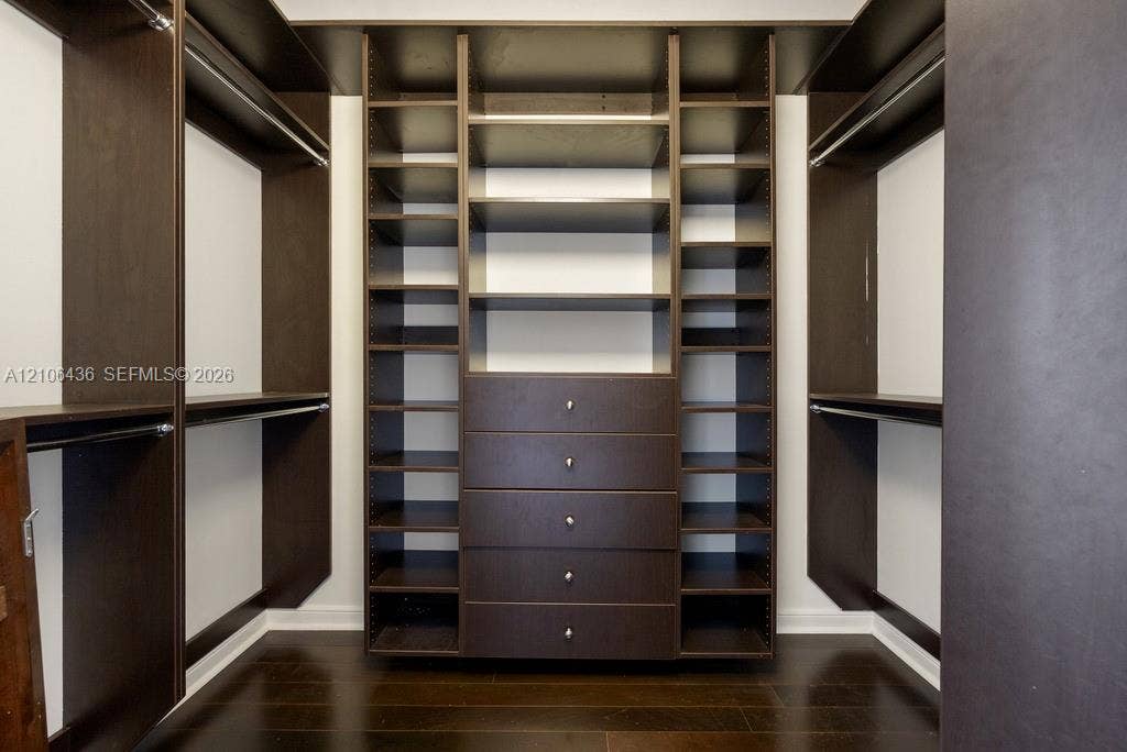 808 Brickell Key Drive, #2102, Miami, Miami, FL 33131 Custom walk-in closet featuring dark wood-finish cabinetry, integrated open shelving, a center bank of five soft-close drawers with metallic pulls, and wood-finish flooring