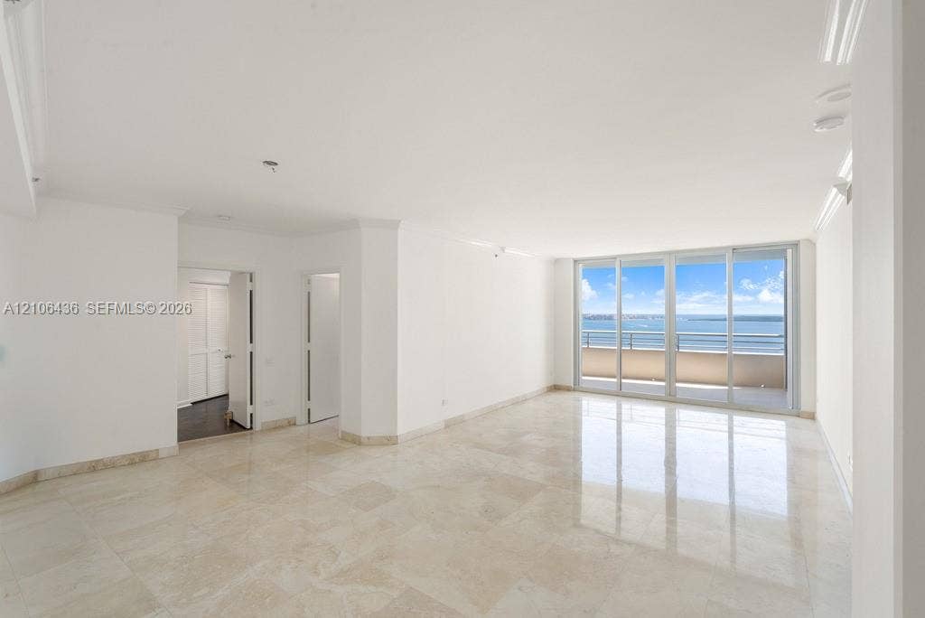 808 Brickell Key Drive, #2102, Miami, Miami, FL 33131 Open-concept interior featuring light-toned stone tile flooring, crown molding, and floor-to-ceiling glass sliding doors providing water scenery and access to a balcony