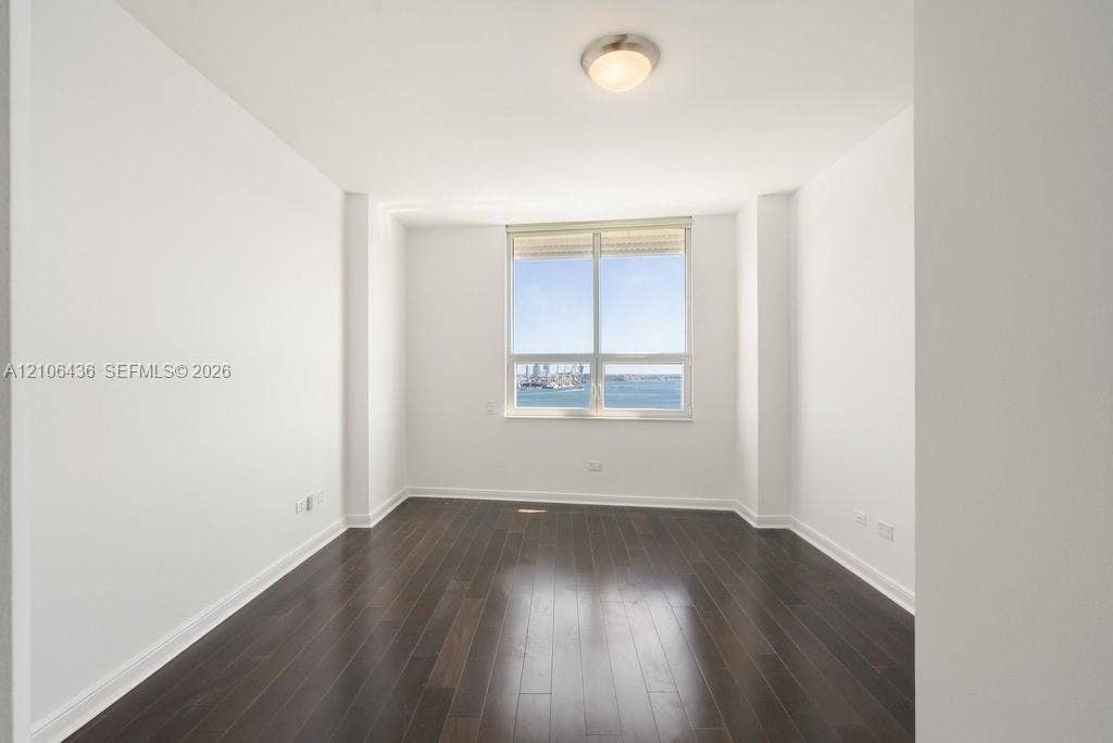 808 Brickell Key Drive, #2102, Miami, Miami, FL 33131 Room featuring wood-finish flooring, white walls, and a large window showcasing water and harbor scenery, complemented by a flush-mount ceiling light fixture
