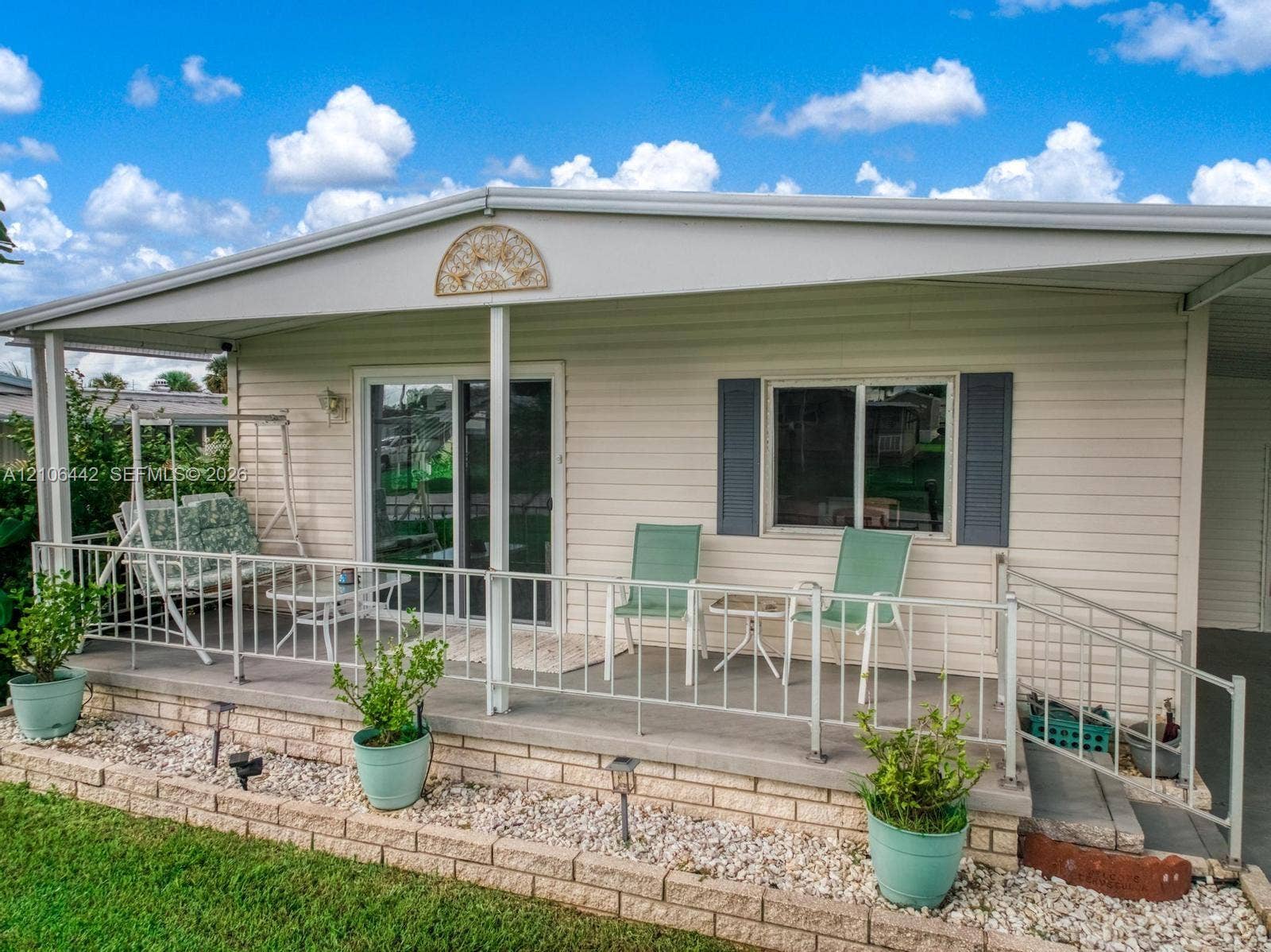 Covered front porch featuring white metal railings, light-colored horizontal siding, brick-veneer base, sliding glass doors, and dark decorative shutters
