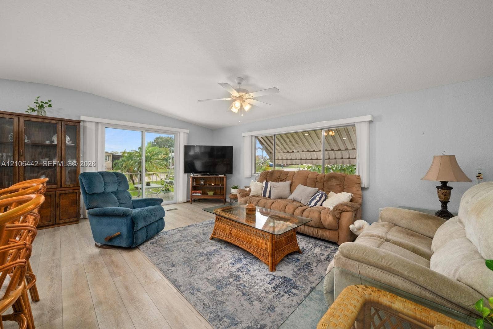 Living area featuring light-toned wood-finish flooring, a ceiling fan with integrated lighting, a sliding glass door, and an exterior retractable window awning