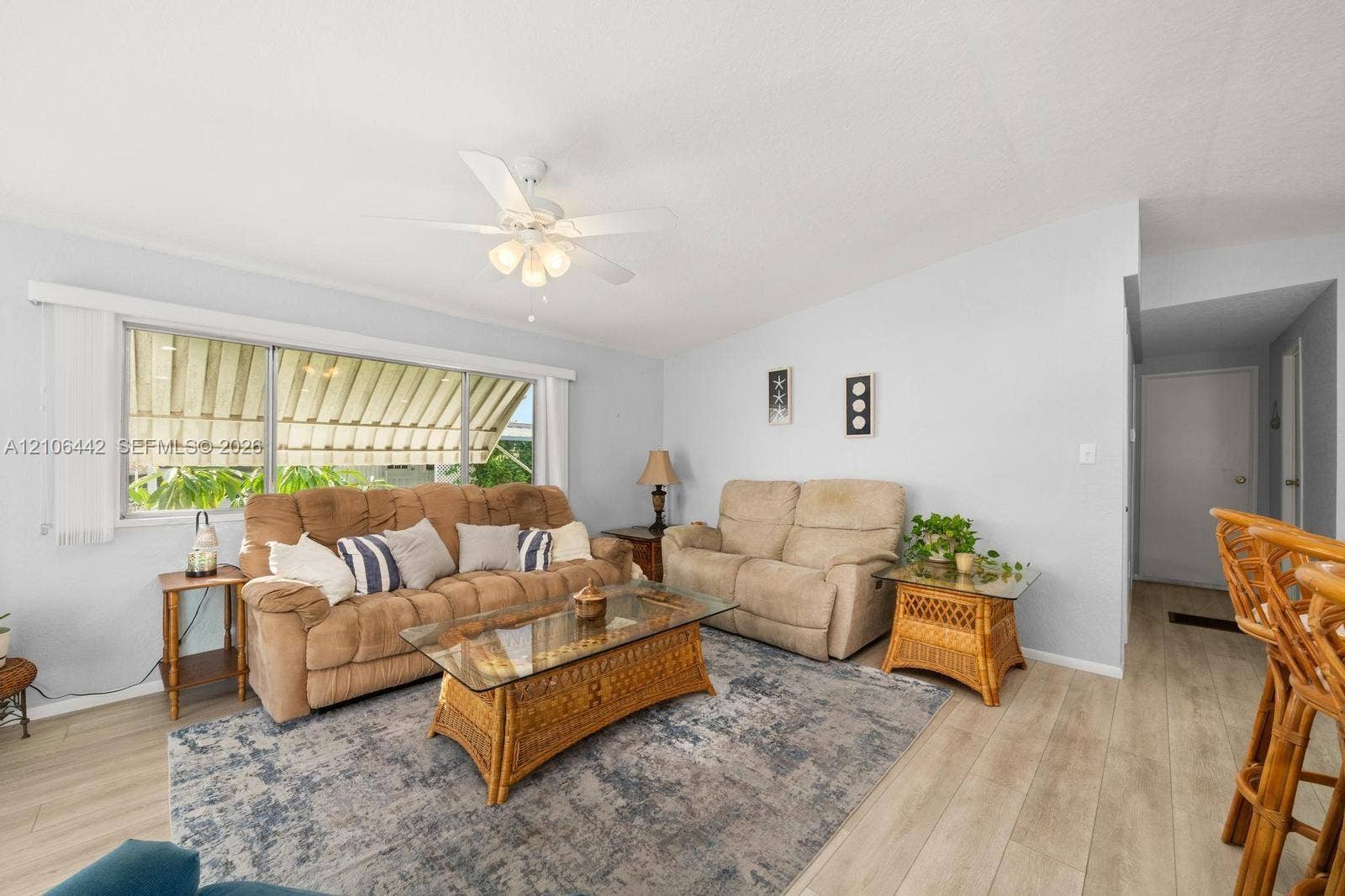 Living space featuring wood-finish flooring, a neutral color palette, a ceiling fan with integrated lighting, and a large window with an exterior metal awning