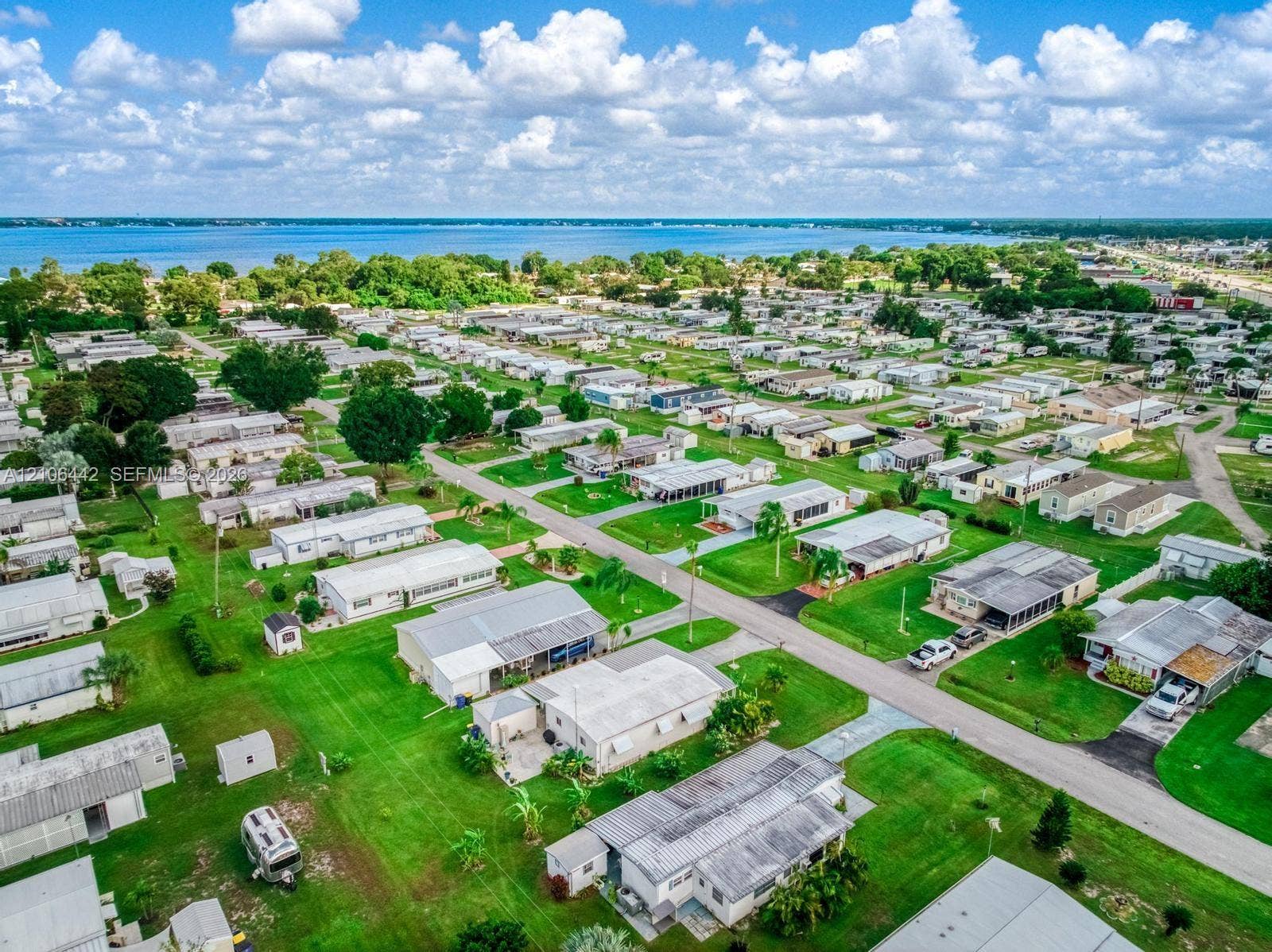Aerial perspective of a residential community featuring expansive green lawns, paved streets, mature trees, and proximity to open water