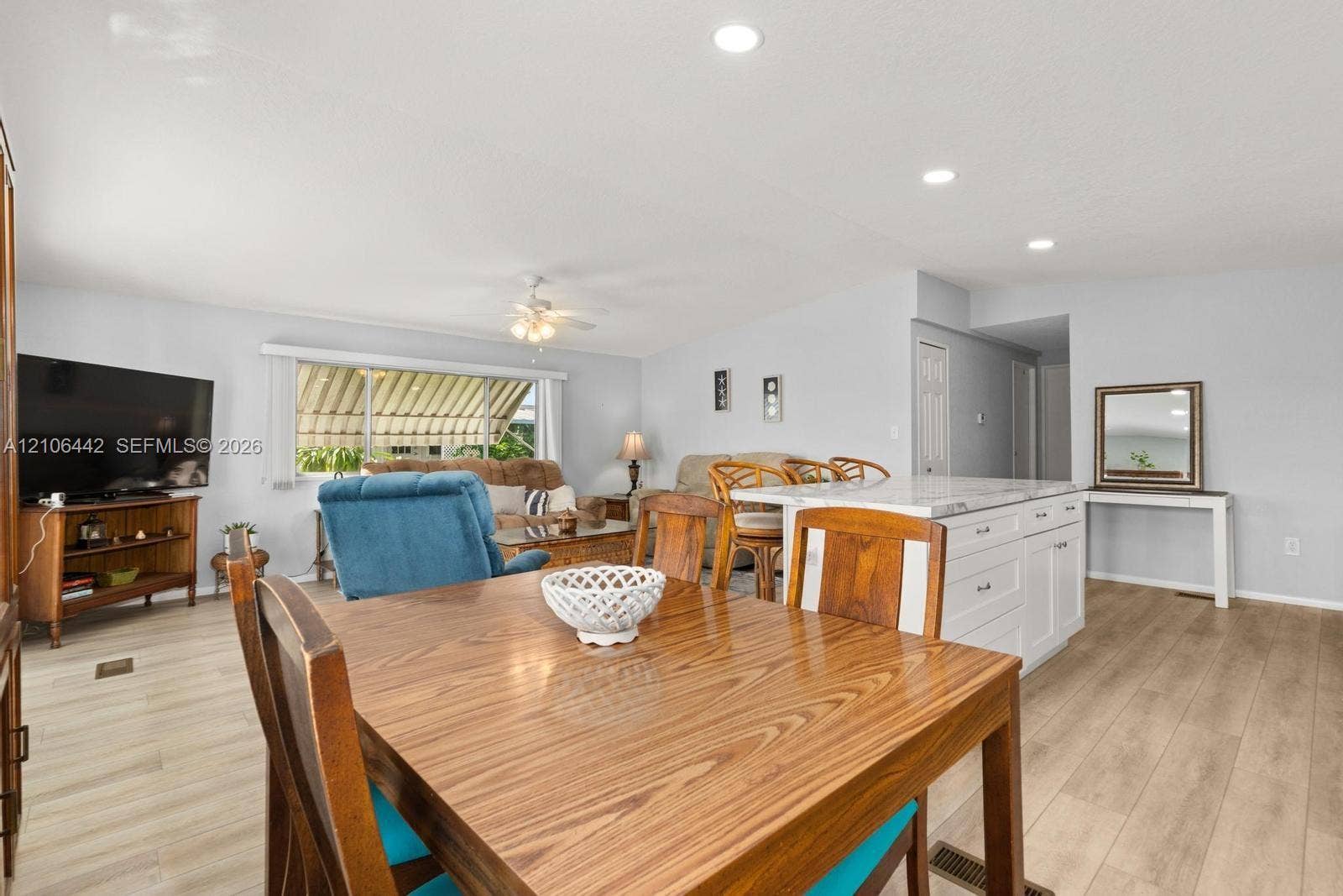 Open-concept interior featuring wood-finish flooring, recessed lighting, and a kitchen island with white cabinetry and a stone-surface countertop