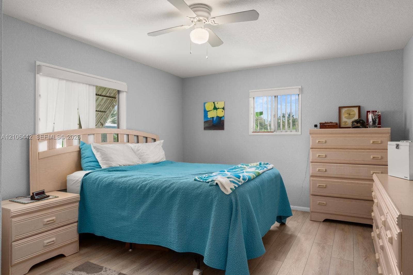 Neutral-toned walls, wood-finish flooring, and a ceiling fan with integrated light fixture, complemented by dual windows