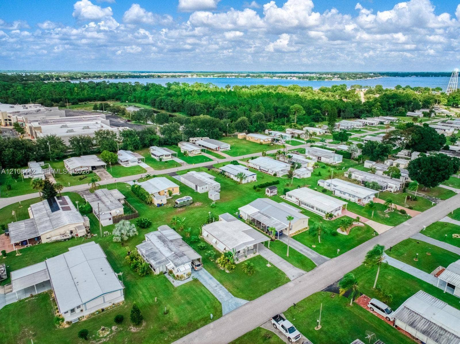 Aerial perspective of a residential community featuring expansive green space, paved street infrastructure, mature trees, and proximity to a large body of water