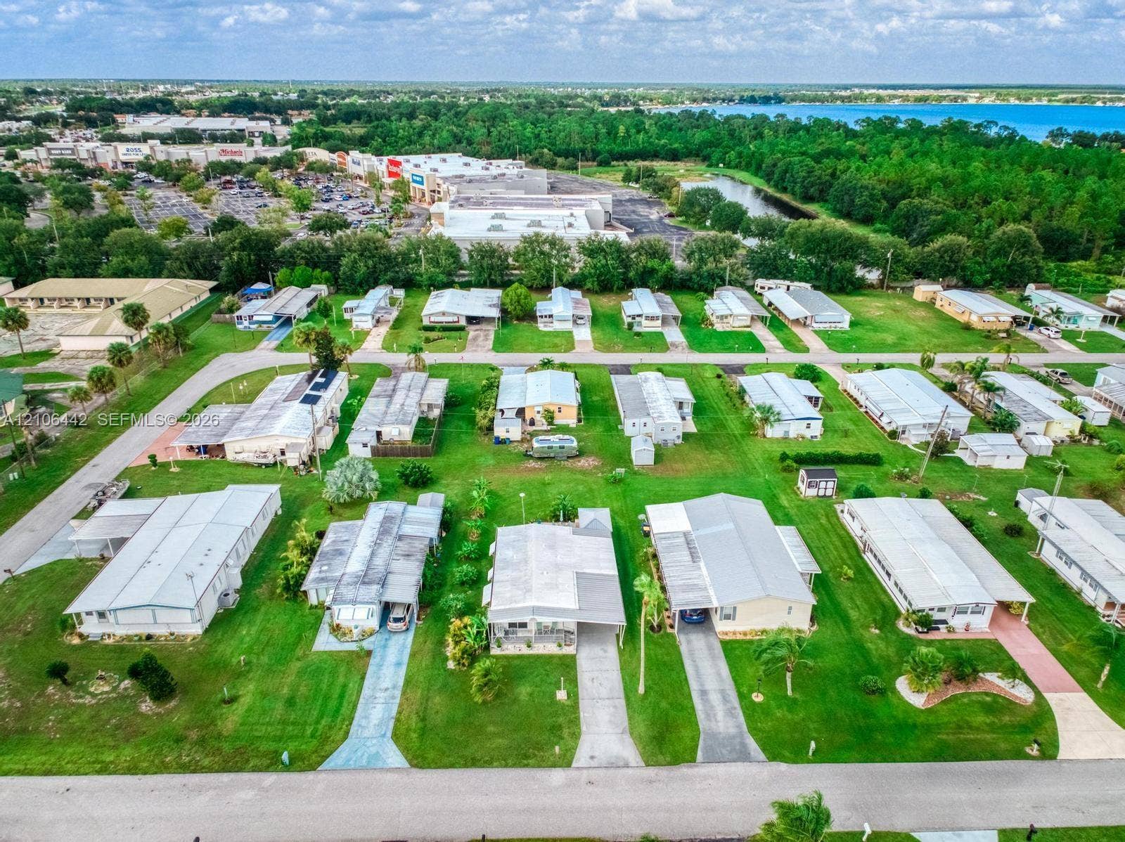 Aerial perspective of residential community featuring paved driveways, manicured lawns, mature palm trees, and proximity to regional retail centers and waterfront scenery