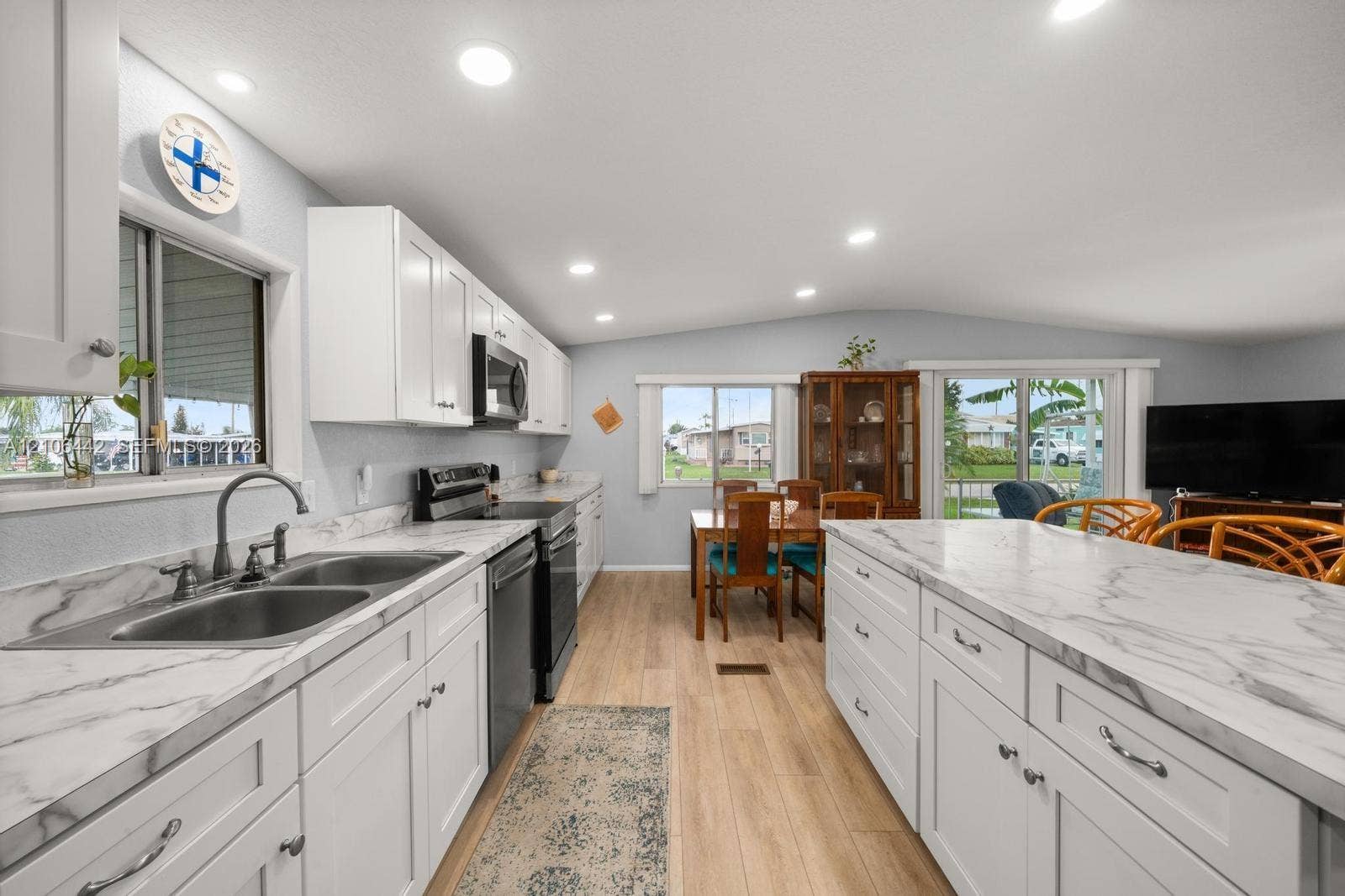 Kitchen featuring white shaker-style cabinetry, solid-surface countertops with a veined pattern, stainless steel double-basin sink, recessed ceiling lighting, and wood-finish flooring