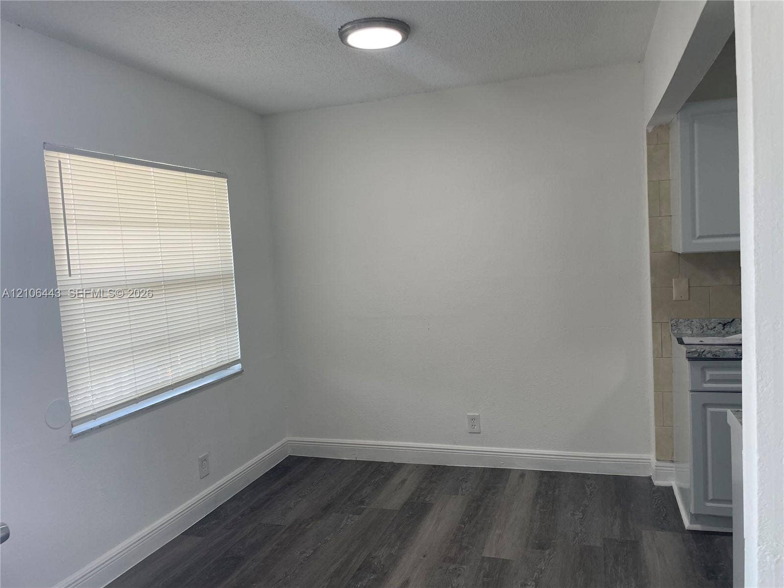 Room featuring wood-finish flooring, a window with installed blinds, and a flush-mount ceiling light fixture, accented by cabinetry with stone-pattern countertops