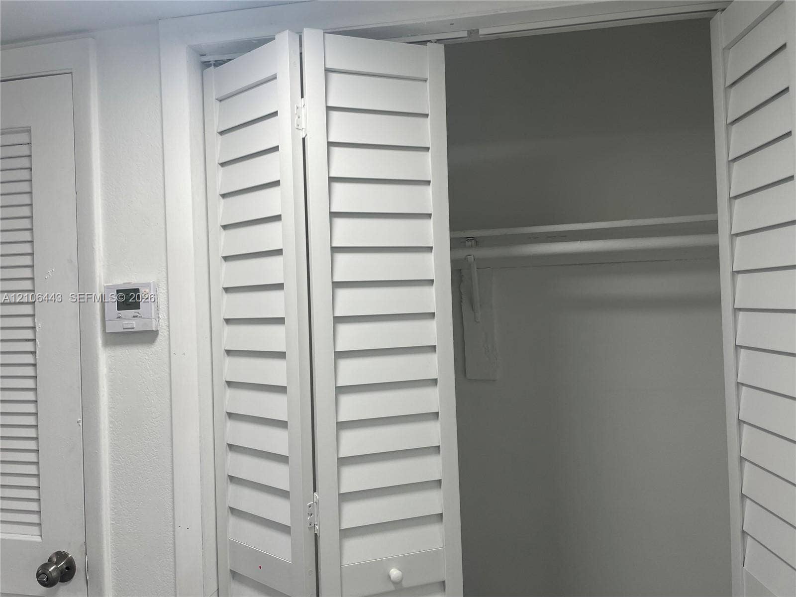 White bi-fold louvered closet doors, interior shelf, and metal garment rod