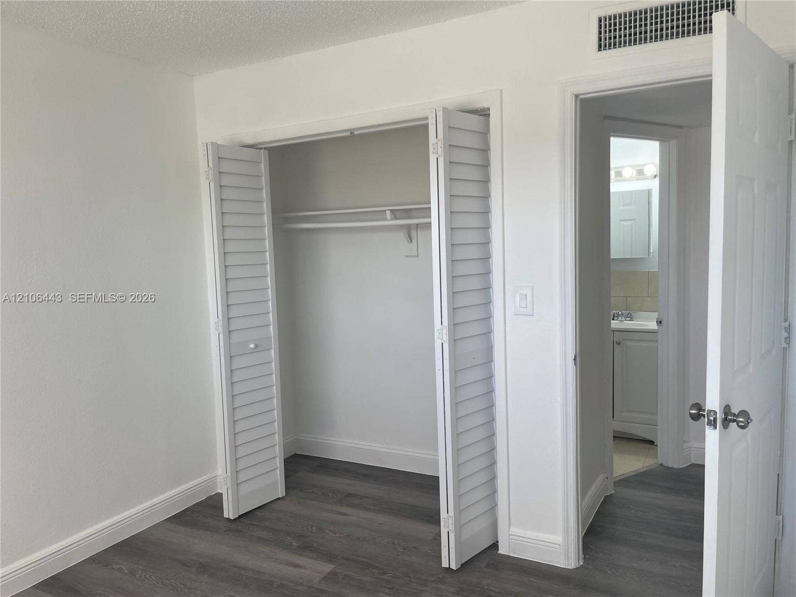 Interior space featuring wood-finish flooring, white louvered closet doors, and solid-core panel doors with brushed nickel hardware
