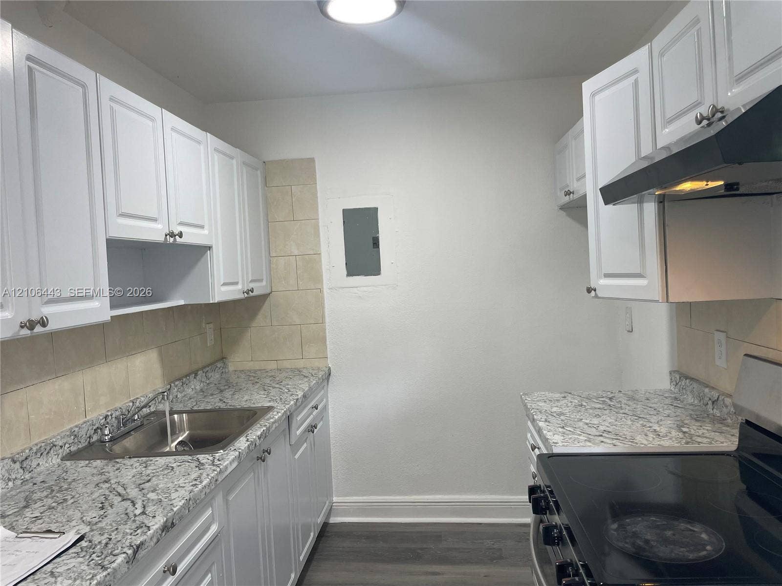 Kitchen featuring white cabinetry, stone-patterned countertops, a stainless steel sink with a mounted faucet, tile backsplash, and wood-finish flooring