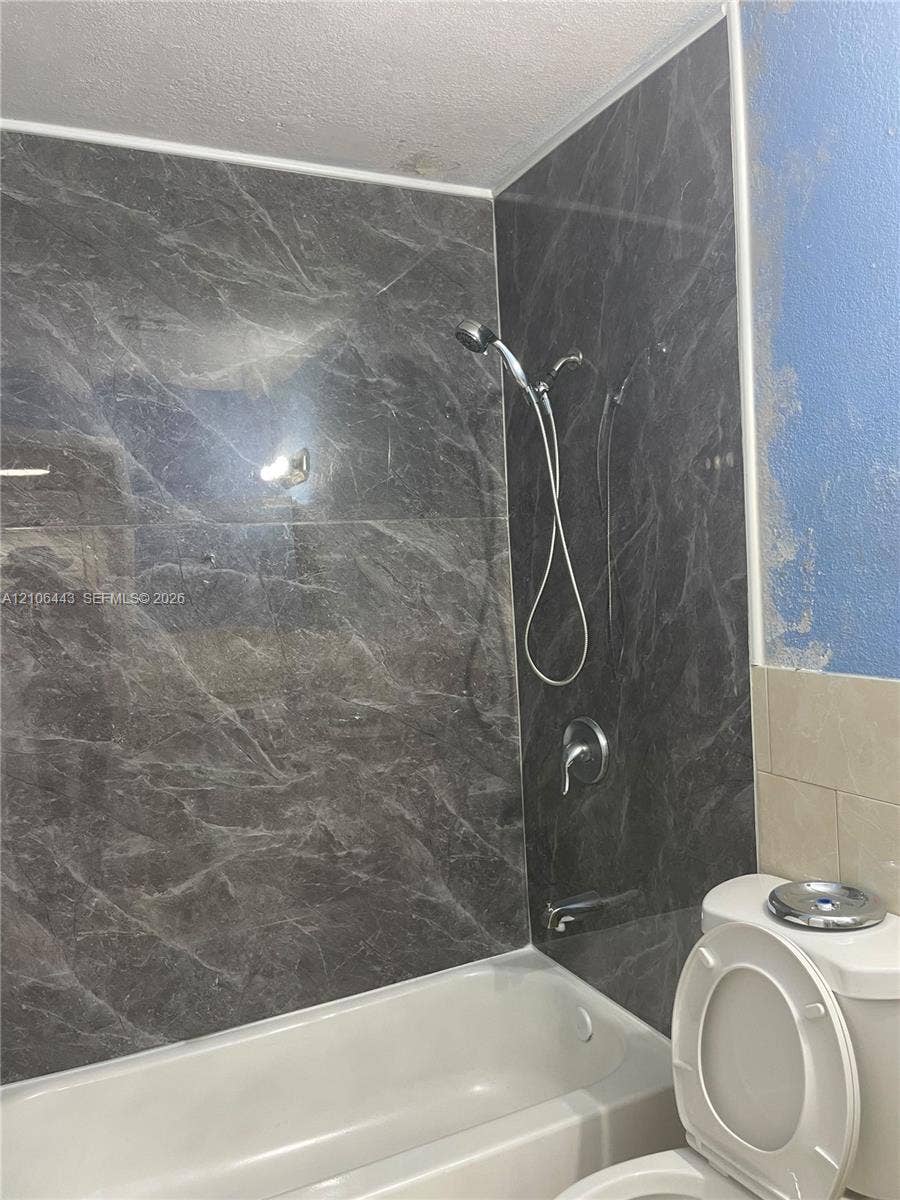 Shower area featuring dark stone-finish wall paneling, a white acrylic tub, and a silver-toned handheld shower fixture
