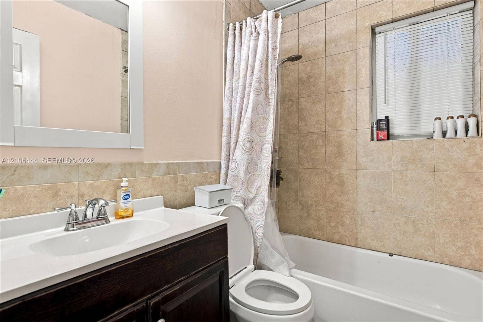 Bathroom featuring a dark wood-finish vanity, solid-surface countertop with an integrated sink, rectangular mirror, and a shower-tub combination with ceramic wall tiling