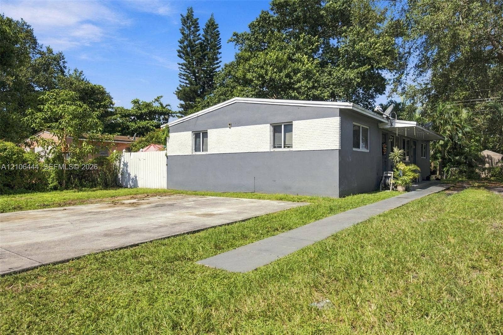 Single-story exterior featuring two-tone stucco siding, a concrete driveway, a concrete walkway, and a white privacy fence