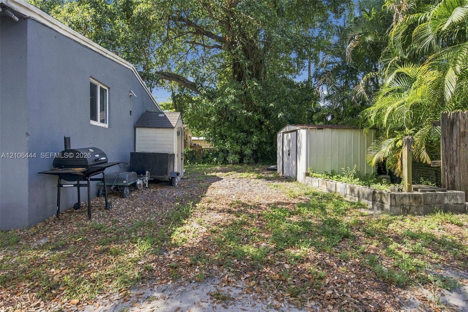 Rear yard featuring mature trees, a detached metal storage shed, and a raised concrete block garden bed