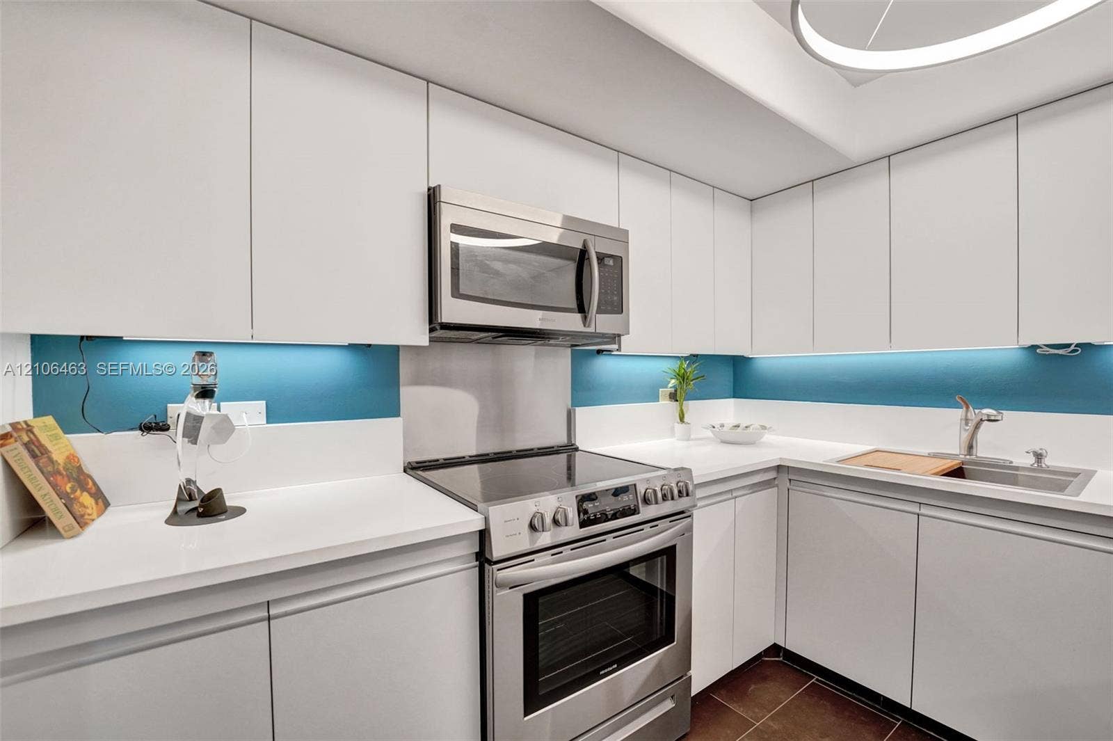 1201 S Ocean Drive, #218N, Hollywood, FL 33019 Kitchen featuring flat-panel white cabinetry, solid surface countertops, stainless steel appliances, integrated under-cabinet lighting, and a circular overhead light fixture