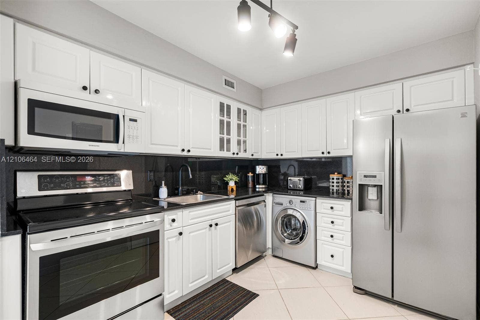 6770 Indian Creek Drive, #8E, Miami Beach, FL 33141 Kitchen featuring white shaker-style cabinetry, high-contrast dark stone countertops, stainless steel appliances, built-in front-load laundry, and tile flooring