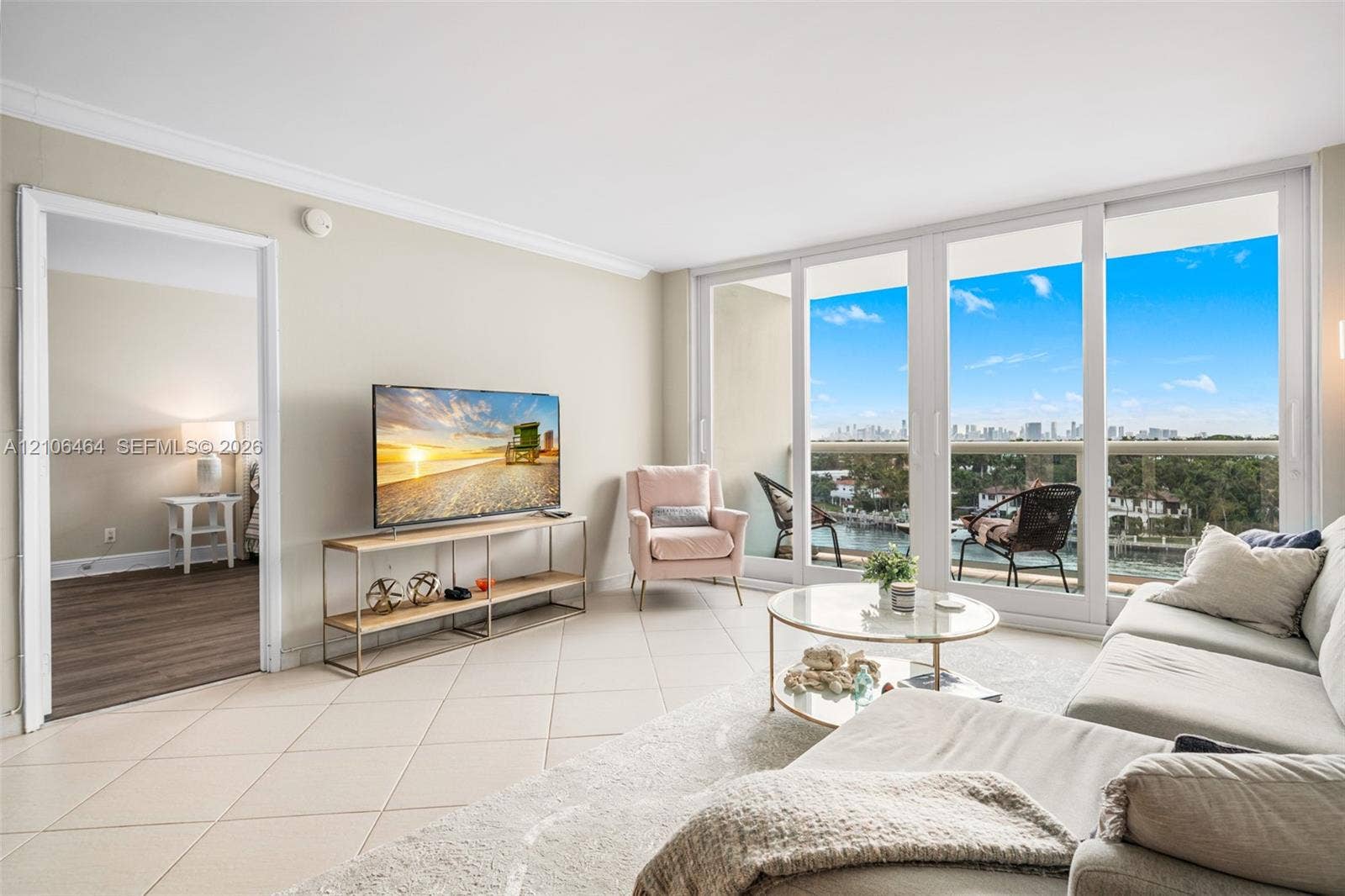 6770 Indian Creek Drive, #8E, Miami Beach, FL 33141 Living area featuring large-format ceramic tile flooring, crown molding, and floor-to-ceiling sliding glass doors opening to a balcony with water and city skyline scenery