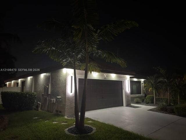 Exterior facade featuring stucco siding, a multi-car garage, recessed soffit lighting, vertical wall-mounted exterior light fixtures, and palm tree landscaping