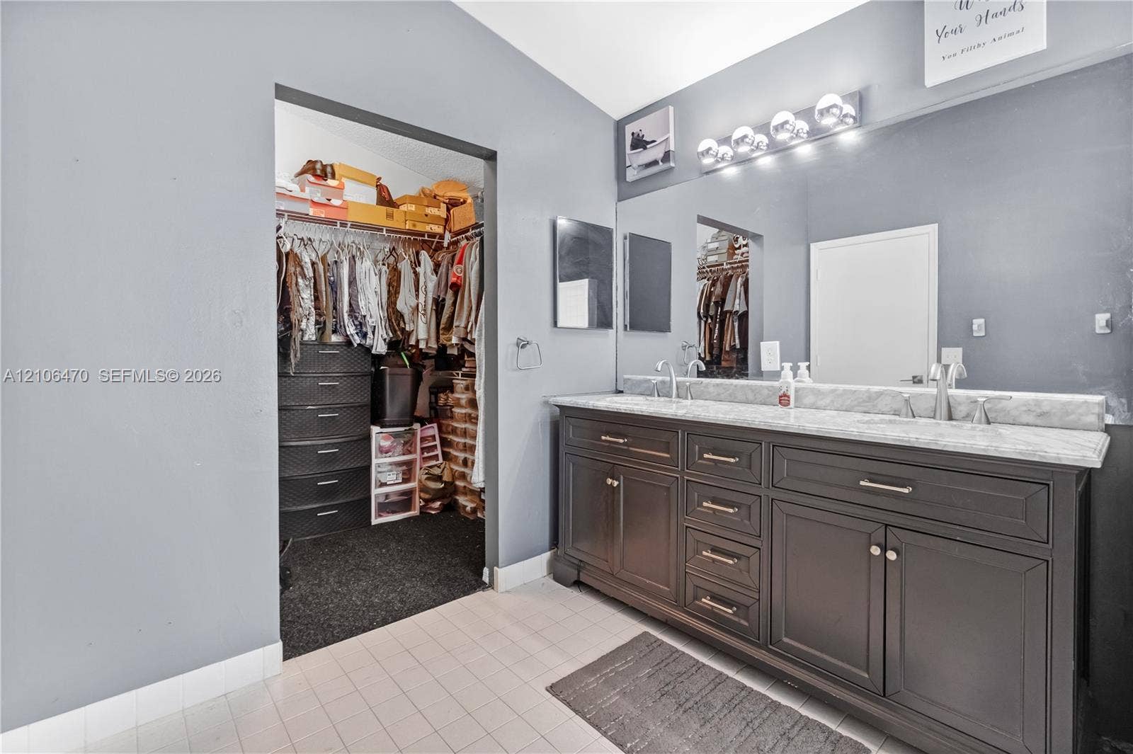 Dual-vanity cabinet with dark finish and light-toned stone countertop, large-format wall mirror, multi-bulb vanity light fixture, and built-in closet storage