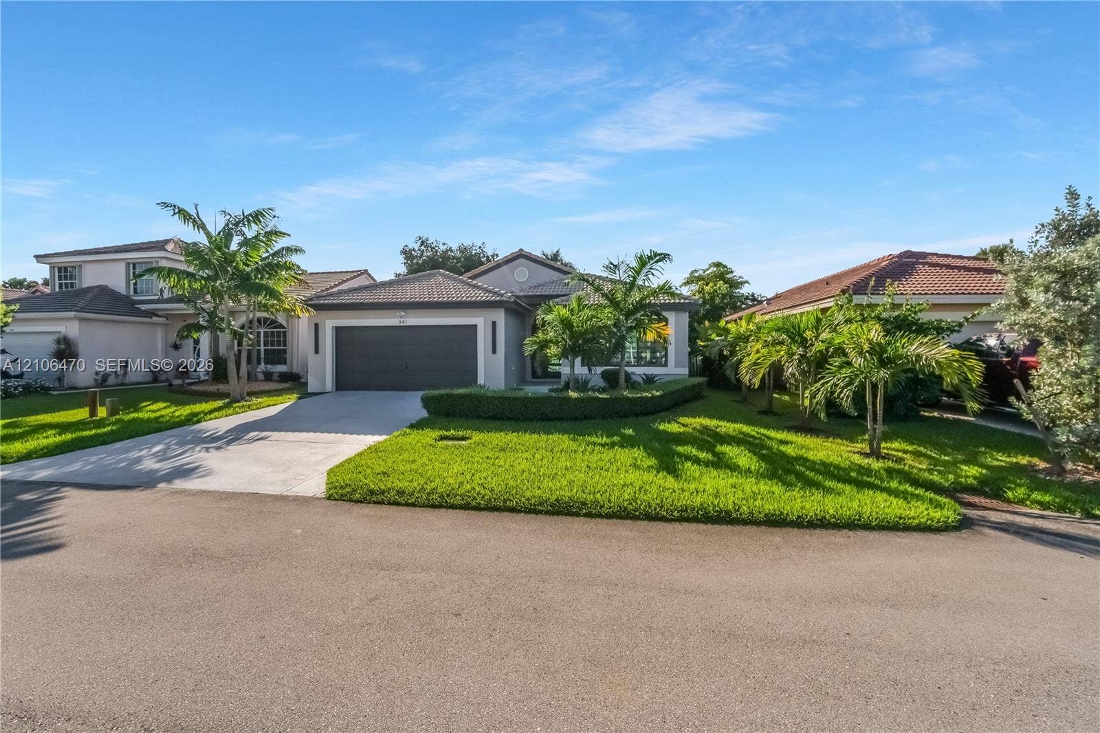 Single-story exterior featuring a concrete tile roof, attached two-car garage, concrete driveway, and manicured landscaping