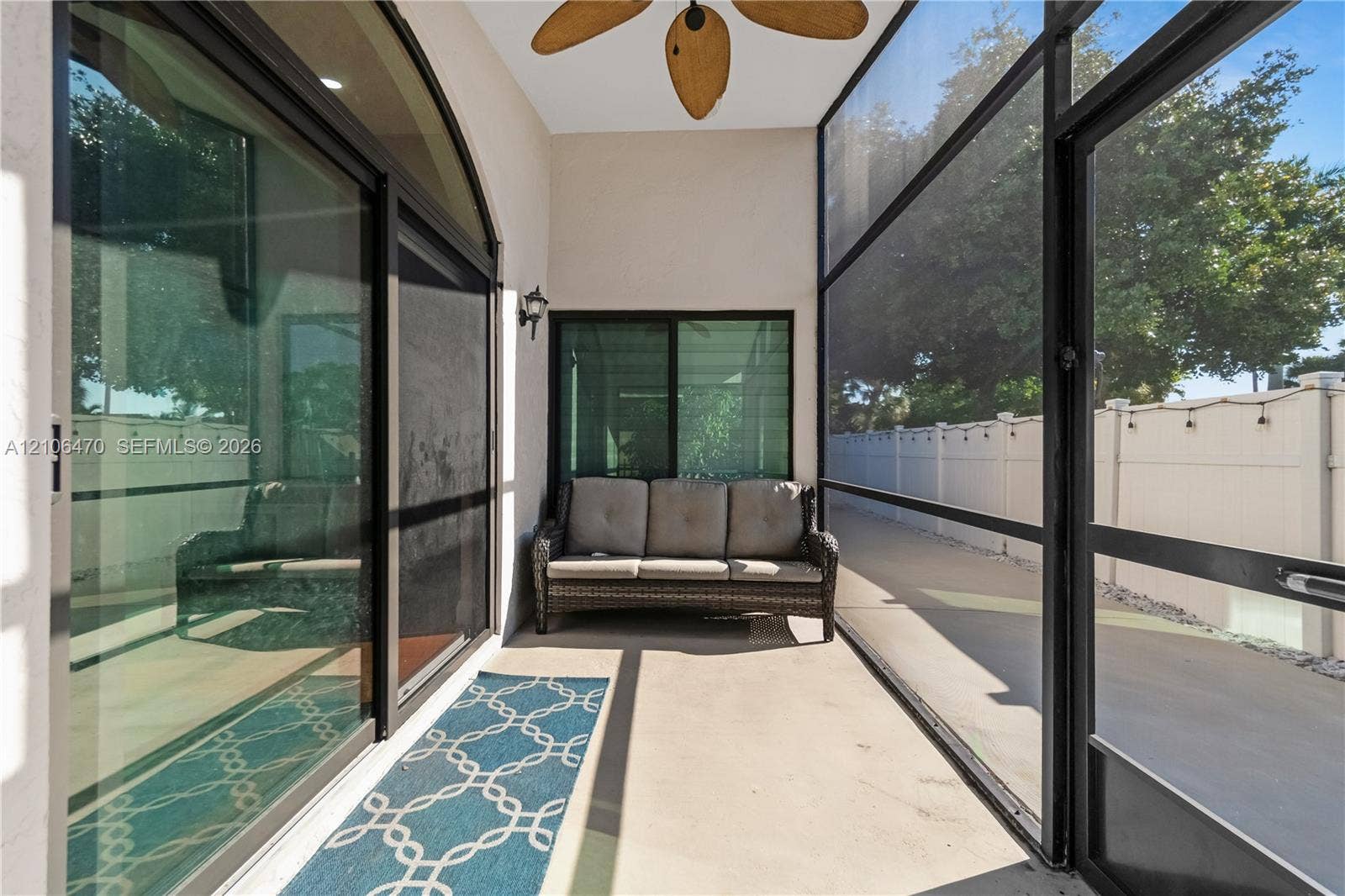 Screened lanai featuring concrete flooring, black-framed sliding glass doors, a ceiling-mounted fan, and an exterior wall light fixture