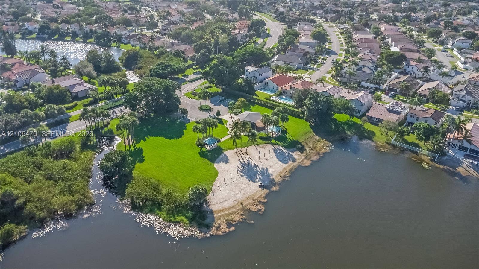 Aerial perspective of a waterfront property featuring a sandy beach, expansive manicured lawn, established palm trees, and a gazebo