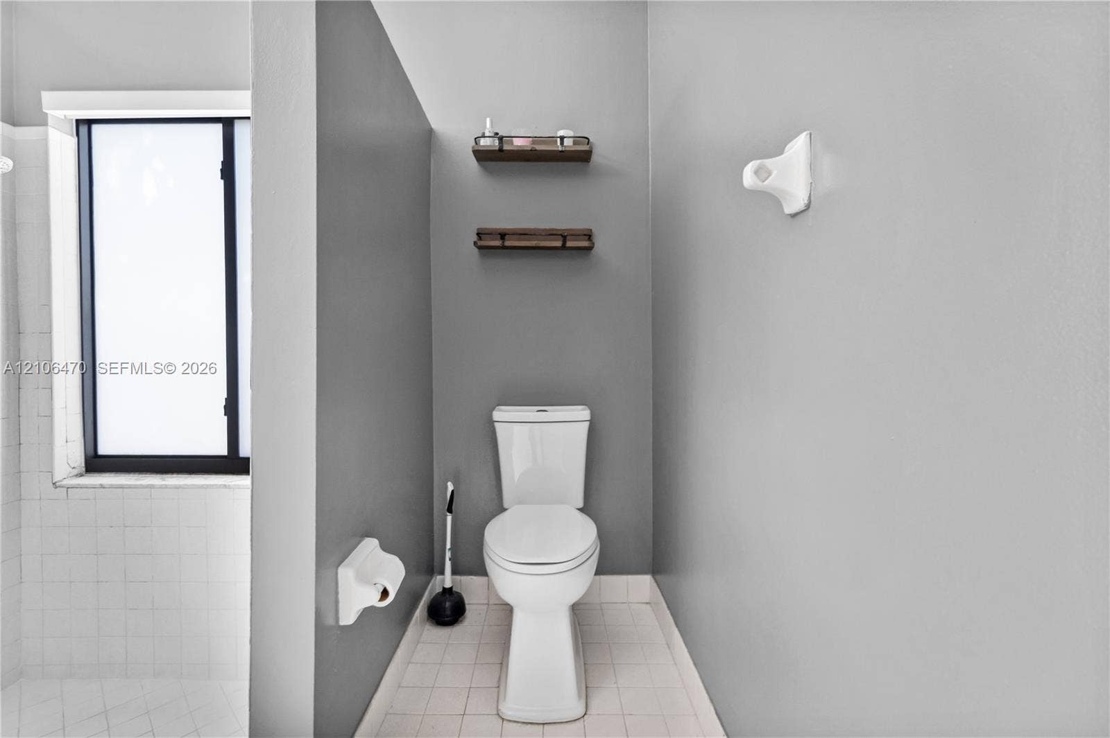 Bathroom featuring dual wood-finish wall shelves, a white vitreous china toilet, and square tile flooring