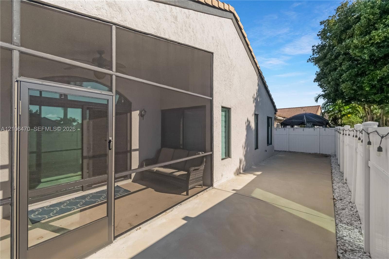 Screened-in lanai featuring a concrete patio, stucco exterior wall, and white vinyl privacy fencing