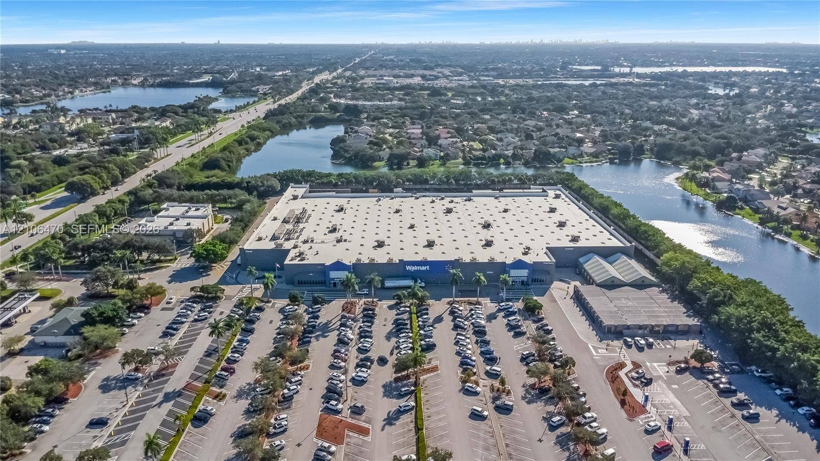 Aerial perspective of a large-scale commercial structure featuring expansive asphalt parking facilities, multiple point-of-entry canopies, and substantial frontage along a primary roadway