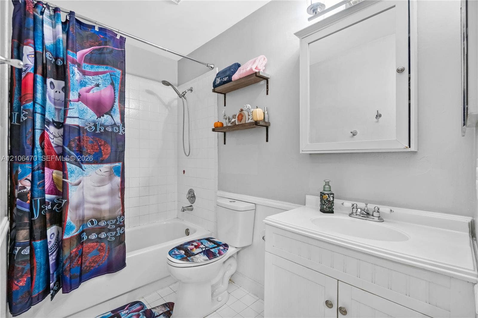 White vanity cabinet with an integrated sink, wall-mounted medicine cabinet, white tile shower surround, and two wood-finish wall-mounted shelves