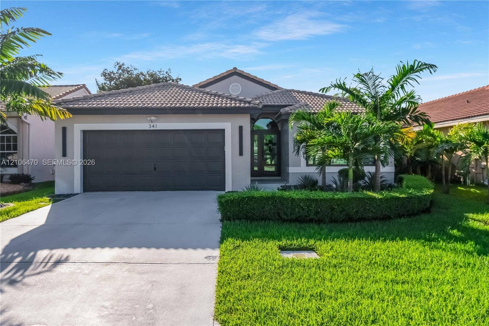 Single-story residence featuring a tile roof, neutral stucco exterior, concrete driveway, attached multi-car garage, and manicured landscaping