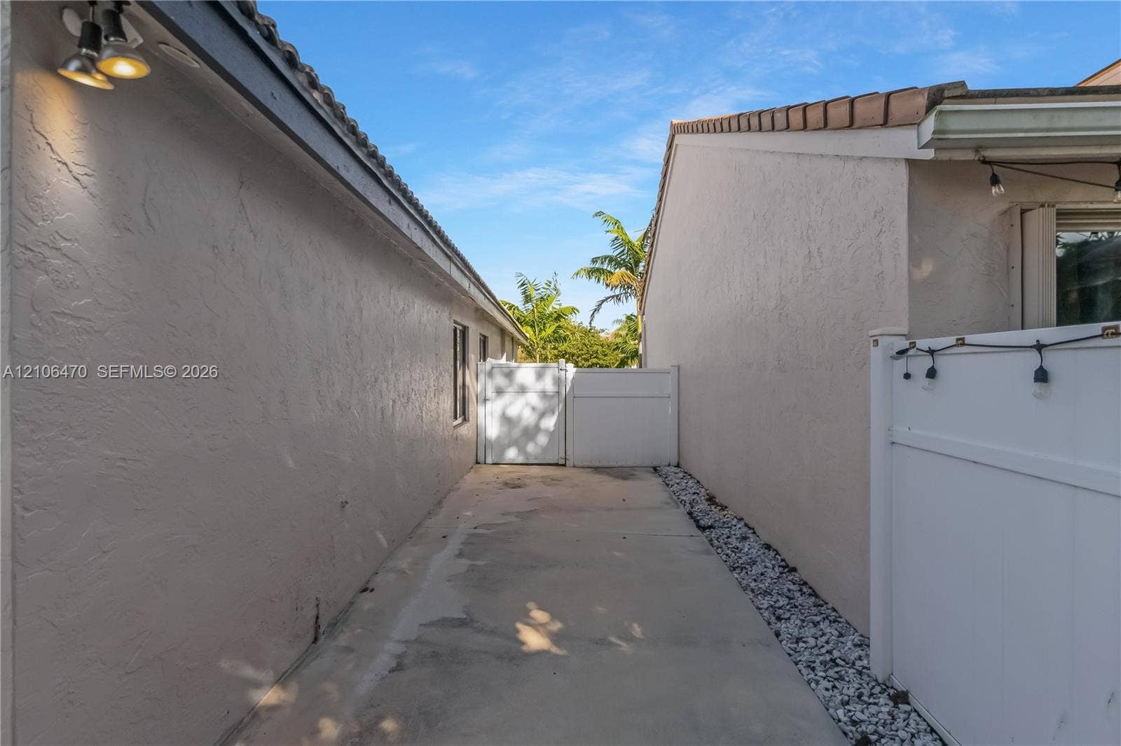 Exterior side yard featuring stucco walls, a concrete walkway, decorative stone border, and a privacy gate