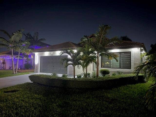 Single-story residence featuring a textured stucco exterior, tile roofing, an integrated two-car garage, and manicured landscaping with mature palms