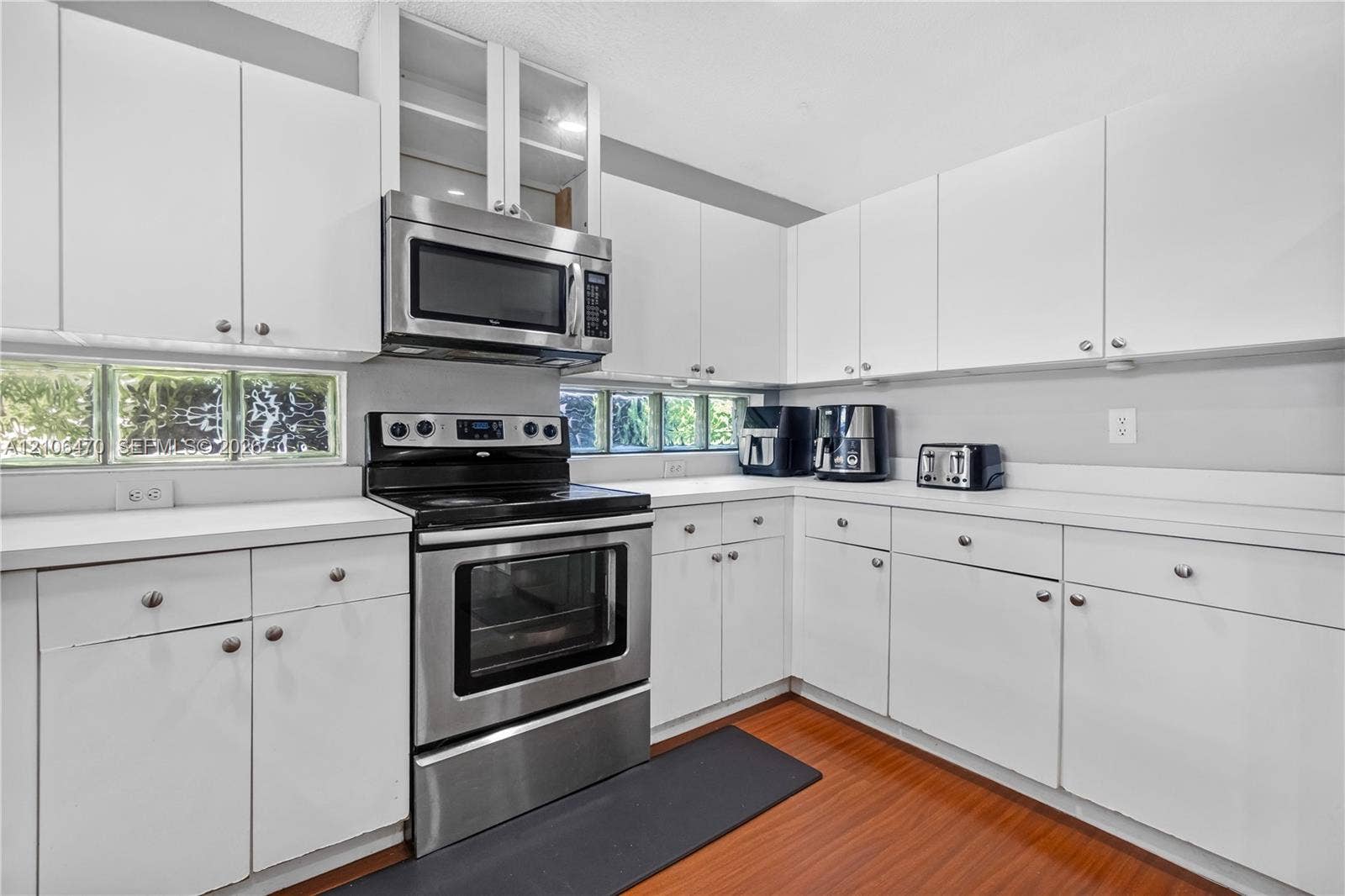 Kitchen featuring white cabinetry, wood-finish flooring, stainless steel appliances, glass block windows, and solid-surface countertops