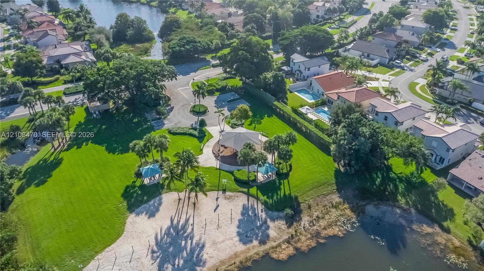 Community park area featuring an expansive lawn, shaded pavilion, sand beach, and mature palm trees situated along the water's edge