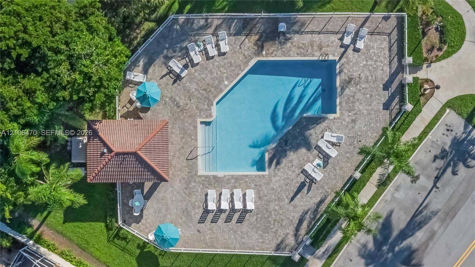Swimming pool with a stone paver deck, covered cabana with a tile roof, perimeter fencing, and surrounding mature landscaping