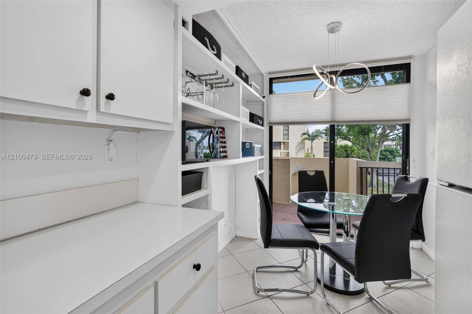 2800 SW 87th Avenue, #1113, Davie, FL 33328 Built-in white cabinetry featuring open shelving, tile flooring, modern sculptural pendant lighting, and sliding glass doors with direct exterior access