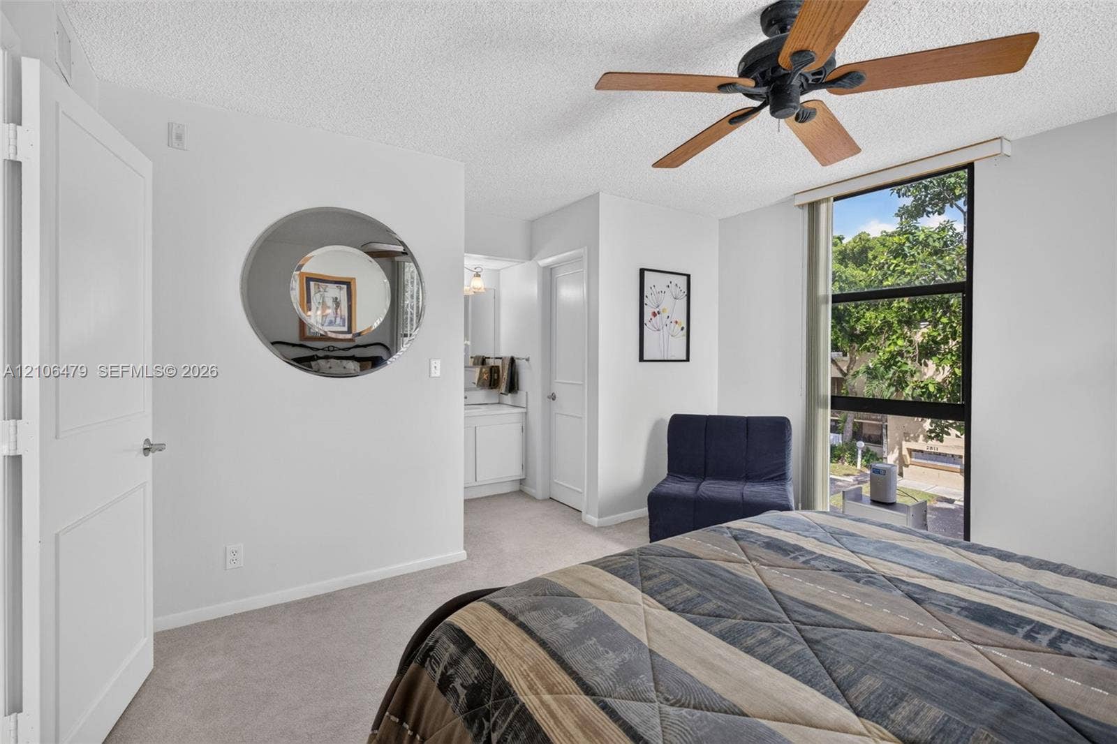 2800 SW 87th Avenue, #1113, Davie, FL 33328 Neutral wall-to-wall carpeting, multi-panel interior door, ceiling fan with wood-finish blades, and large fixed-pane window with black framing