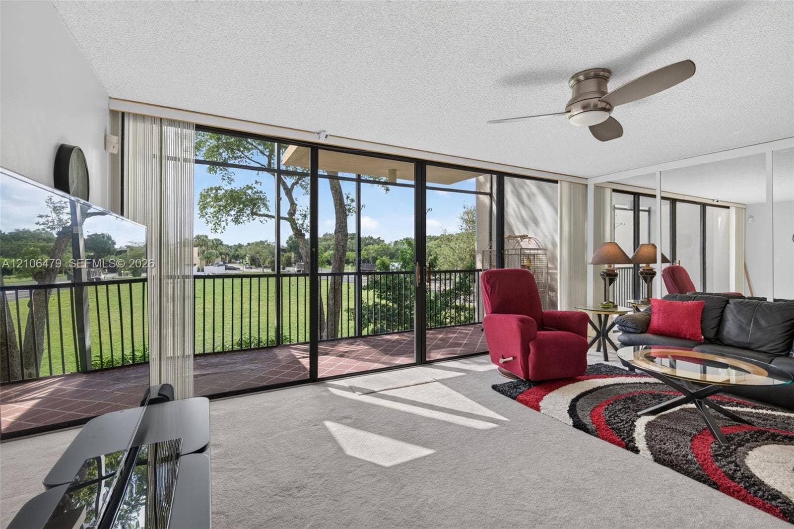 2800 SW 87th Avenue, #1113, Davie, FL 33328 Floor-to-ceiling sliding glass doors opening to a screened balcony, mirrored wall panels, and a central ceiling fan