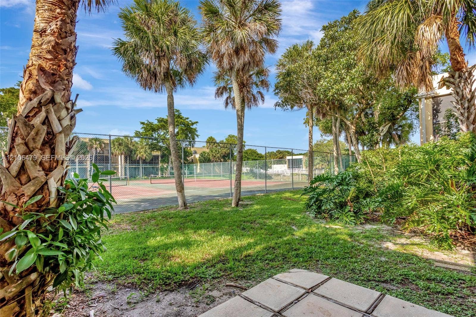 2800 SW 87th Avenue, #1113, Davie, FL 33328 Tennis court with a chain-link fence, concrete patio pavers, and mature palm trees